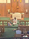Children sit on the floor in a church sanctuary near the altar while adults sit in pews.