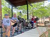 Three musicians playing guitar and drums on a covered outdoor stage.