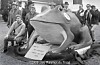Large frog sculpture outdoors with people standing and sitting around it.