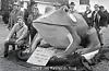Large frog sculpture outdoors with people standing and sitting around it.