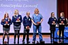 Several people stand on a stage holding awards in front of a blue backdrop.