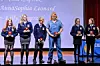 Several people stand on a stage holding awards in front of a blue backdrop.