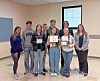 A group of students standing in a classroom holding framed awards and certificates.