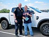 Two men standing beside a white pickup truck in an outdoor parking area.