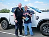 Two men standing beside a white pickup truck in an outdoor parking area.