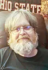 Bearded man with glasses seated indoors in front of an Ohio State sign.