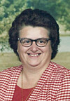 Smiling woman wearing glasses and a red-and-white checkered top in front of a blurred green background.