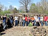 A group of volunteers stands outdoors near trees and stone walls with bags and cleanup tools.