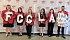 Group of people holding large letters and a 'Live life in red' sign in front of a branded backdrop.