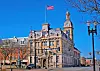 Historic stone building with a clock tower and an American flag flying above it.