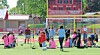 Children on a soccer field with cones, balls, and training equipment near a goal and scoreboard.