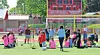 Children on a soccer field with cones, balls, and training equipment near a goal and scoreboard.