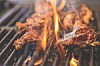 Two steaks grilling over open flames on metal grates.