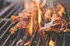Two steaks grilling over open flames on metal grates.