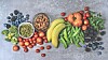 Top-down view of assorted fruits and vegetables arranged on a gray surface.