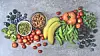 Top-down view of assorted fruits and vegetables arranged on a gray surface.