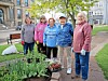 Five people standing next to a flower and vegetable bed in a small urban garden area.