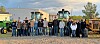 Group of people standing in front of tractors and farm equipment outdoors.