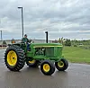 Green John Deere tractor with yellow wheels on wet pavement beside a grassy area.