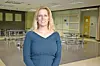 Woman standing in front of tables and chairs inside an empty cafeteria.