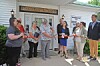 Group of people stands outside a Fredericktown building holding a red ribbon during a ribbon-cutting ceremony.