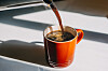 Coffee pours into an orange mug on a bright surface.