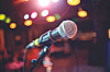 Close-up of a microphone on a stand with out-of-focus colorful lights behind it.