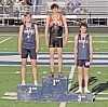 Three athletes stand on first, second, and third place podium blocks at a track stadium.