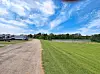 A gravel path curves past a grassy field with trees under a blue sky with scattered clouds.