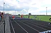 Athletes compete in a hurdle race on an outdoor track beside a fenced spectator area.