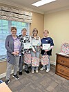 Four women stand together in an office holding framed certificates.