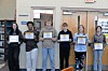 Six students stand in a school hallway holding certificates.