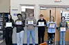 Six students stand in a school hallway holding certificates.
