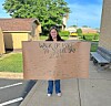 Person holding a handwritten Walk or Bike to School Day 2024 sign on a sidewalk.