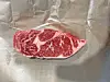 A raw marbled steak placed on wrinkled parchment paper.