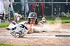 Baseball player sliding headfirst into home plate with dust kicked up on a dirt field.