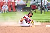 Baseball player sliding headfirst on a dirt infield near a base.