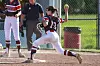 Softball pitcher mid-throw on a dirt field with teammates and an umpire behind her.