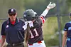 Youth baseball player in a dark uniform raises an arm near an umpire on the field.