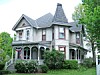 Victorian-style house with a porch, gabled roof, and shrubs in front.