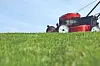 Red ride-on lawn mower in tall green grass with blue sky above.