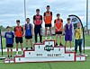 Young athletes stand on a boys pole vault podium at an outdoor track and field meet.