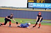 Softball runner slides toward a base while two fielders attempt a tag on the infield.