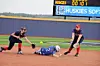 Softball runner slides toward a base while two fielders attempt a tag on the infield.
