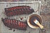 Two racks of glazed ribs on a grill next to a bowl of sauce and a basting brush.