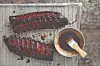 Two racks of glazed ribs on a grill next to a bowl of sauce and a basting brush.