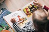 Child viewing an open illustrated picture book on the floor.