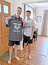 Two people indoors hold up a gray shirt with kidney donor text.