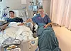 Two patients seated in hospital beds in a hospital room with medical equipment and curtains.