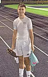 Young athlete standing on a track holding shoes and a bag.
